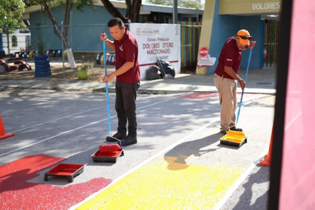 Personal del Imdut pintando un paso peatonal frente al preescolar con niños